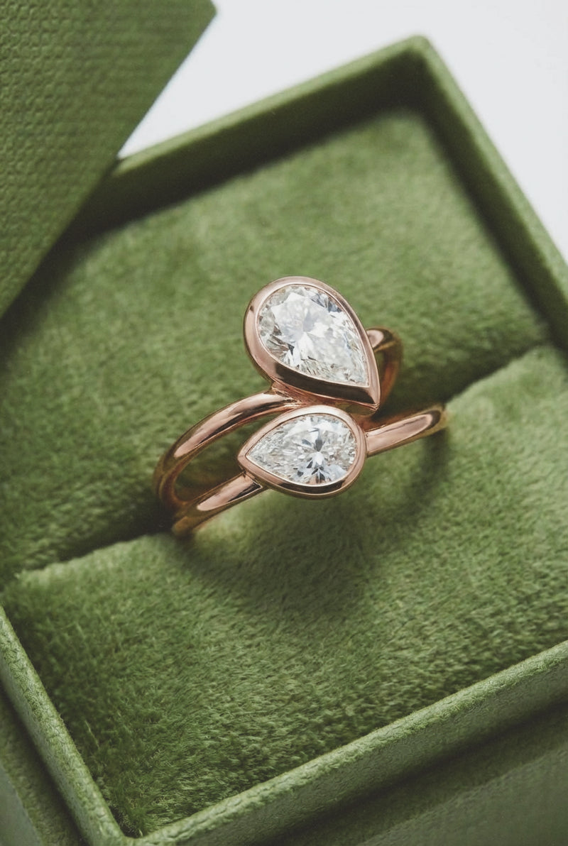 Rose gold ring with two pear-shaped diamonds in a green jewelry box