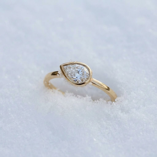 Gold ring with a teardrop-shaped diamond on a snowy background